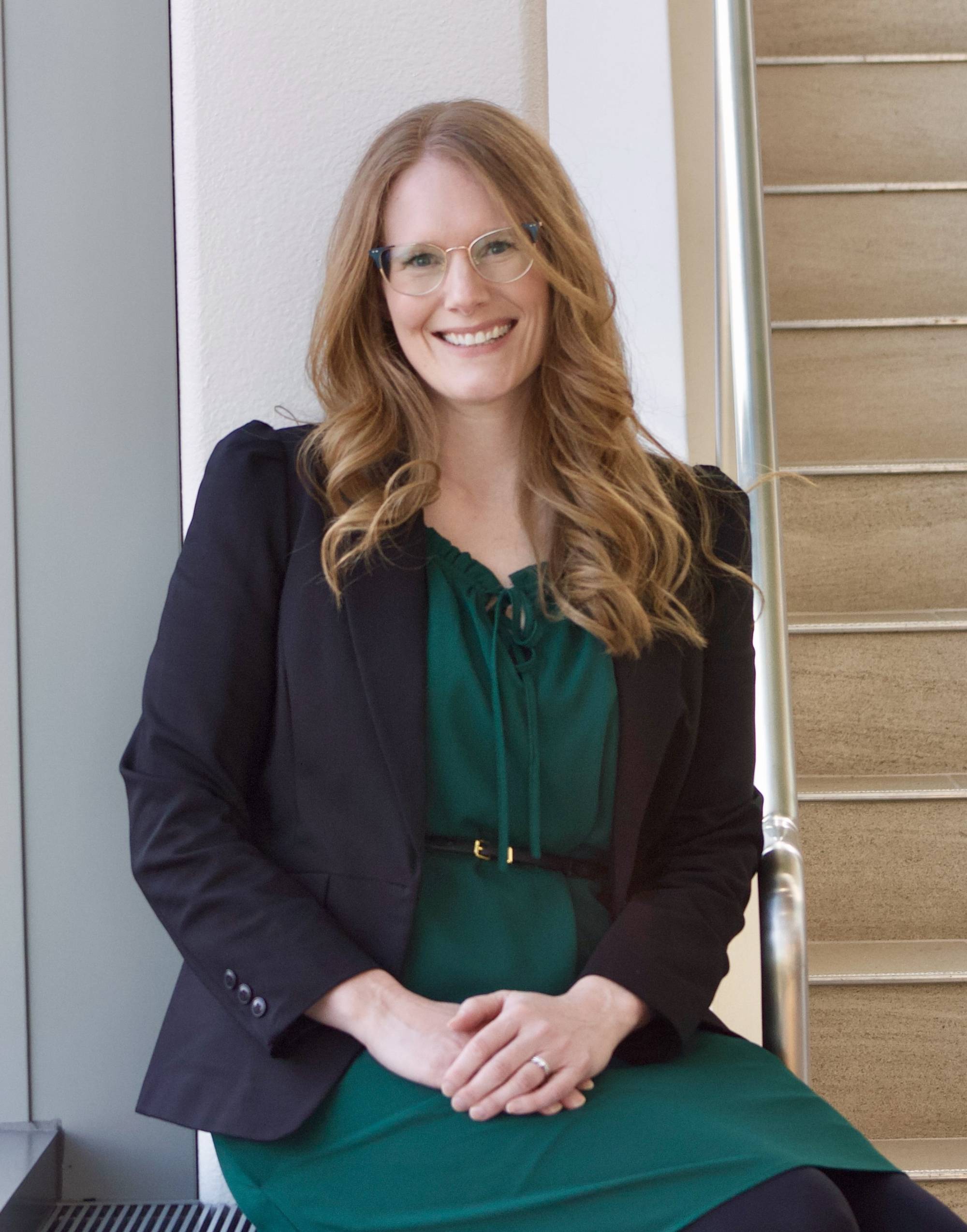 Alexis who has curly red hair, glasses, and is wearing a black blazer and a green blouse